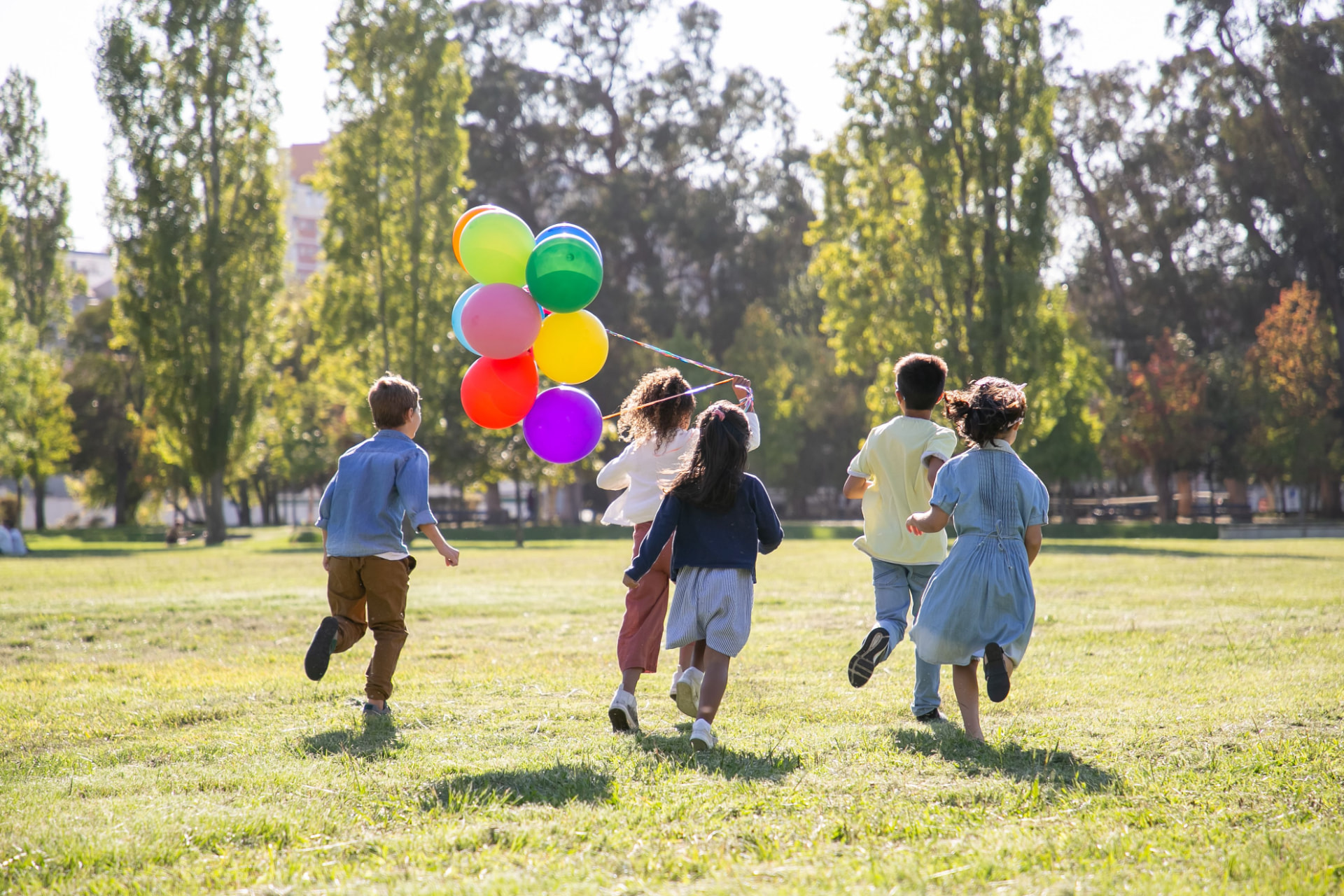 A group of kids running through a park with colorful balloons
