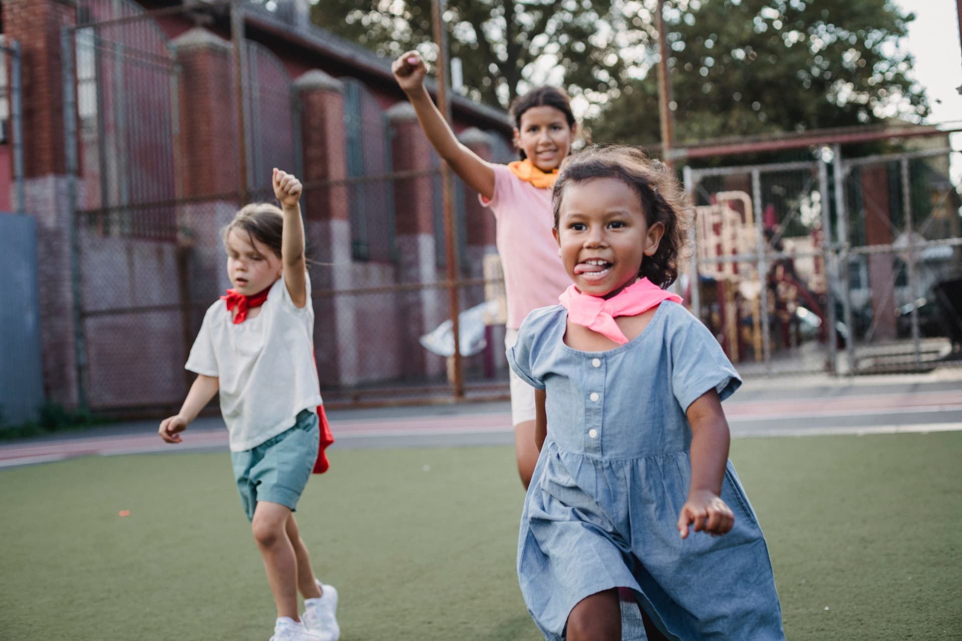 Kids in capes racing across a playground field, laughing