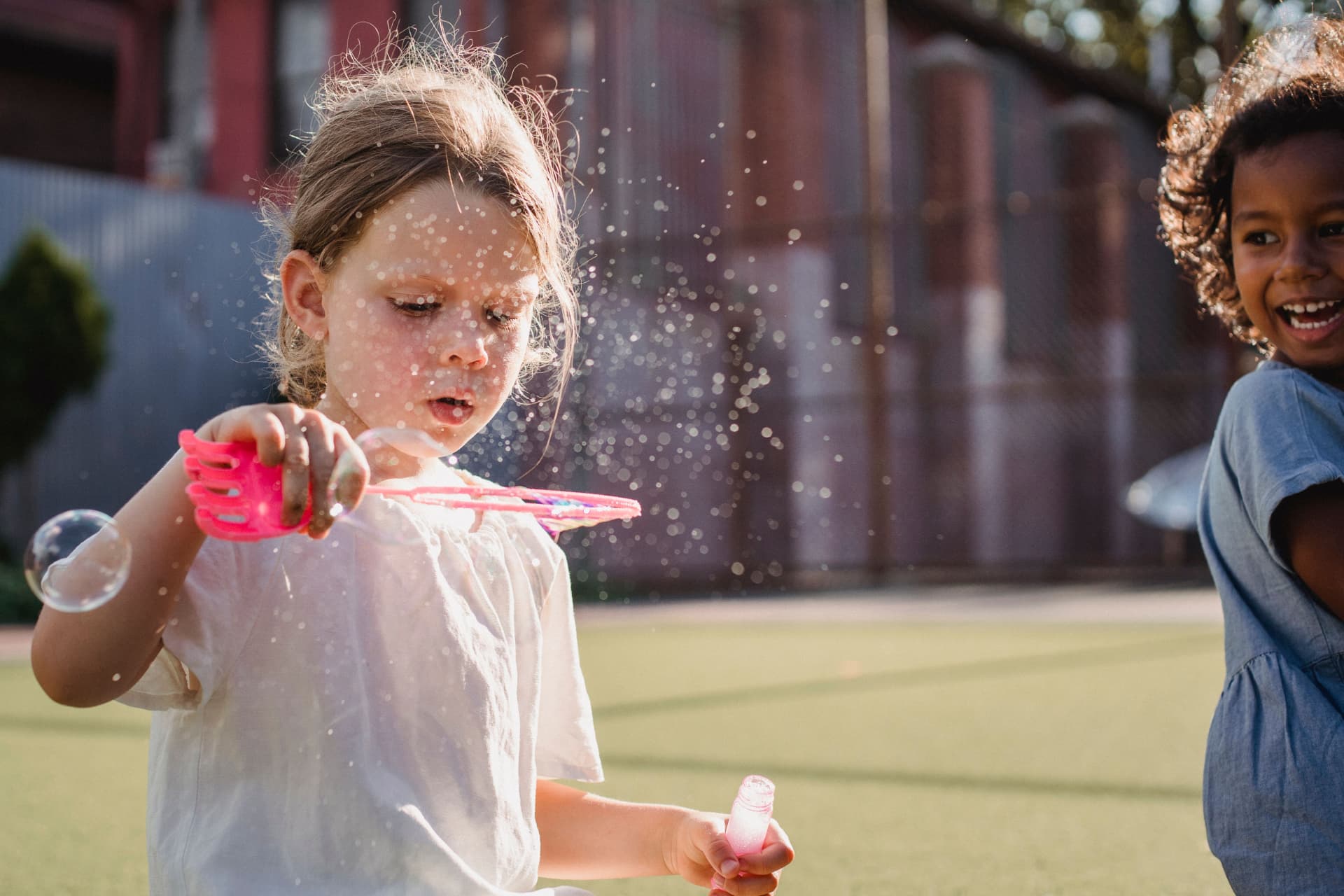 A girl blowing an enormous bubble while a friend laughs beside her