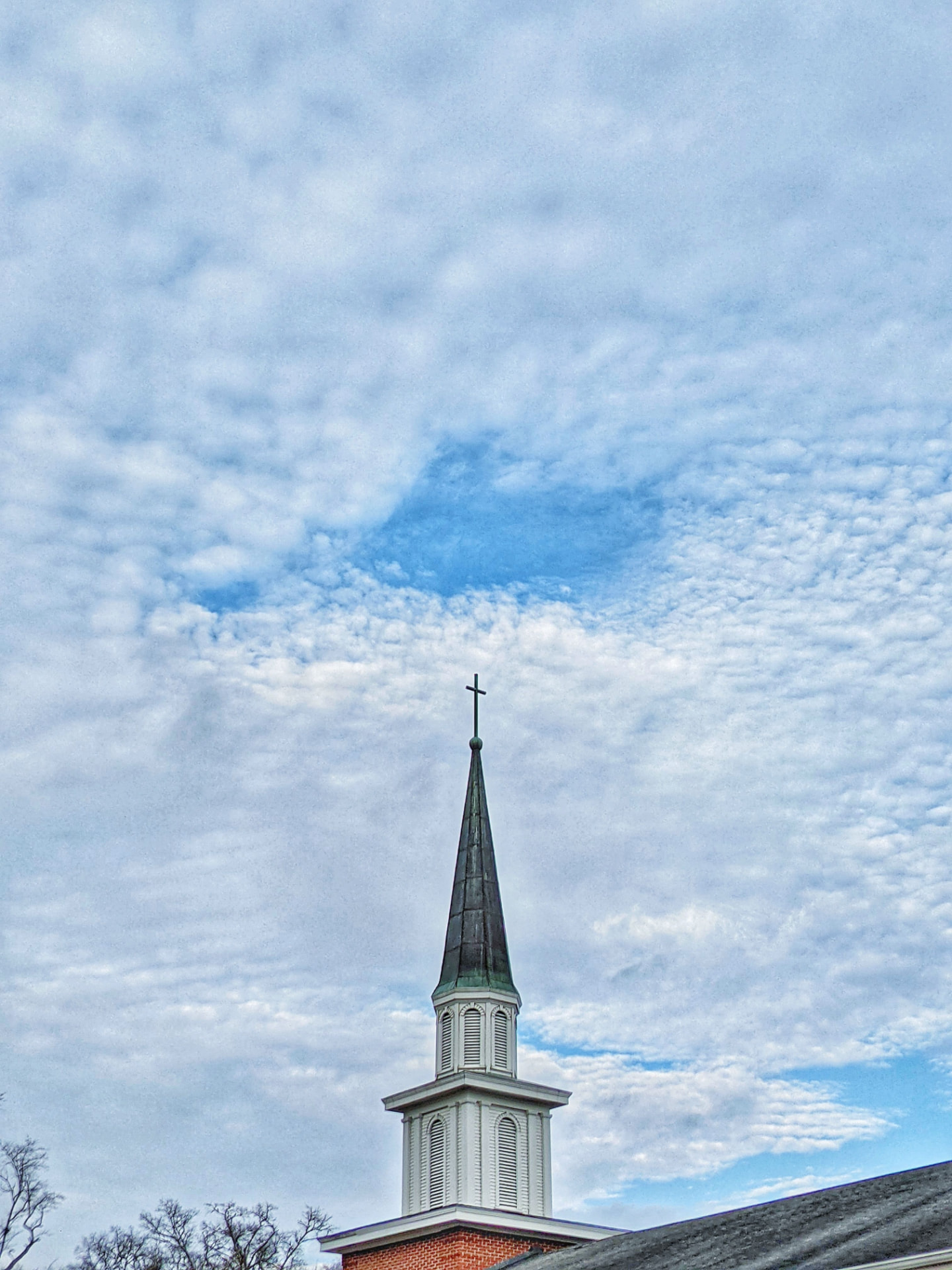 A church steeple reaching into a wide, cloud-dappled sky
