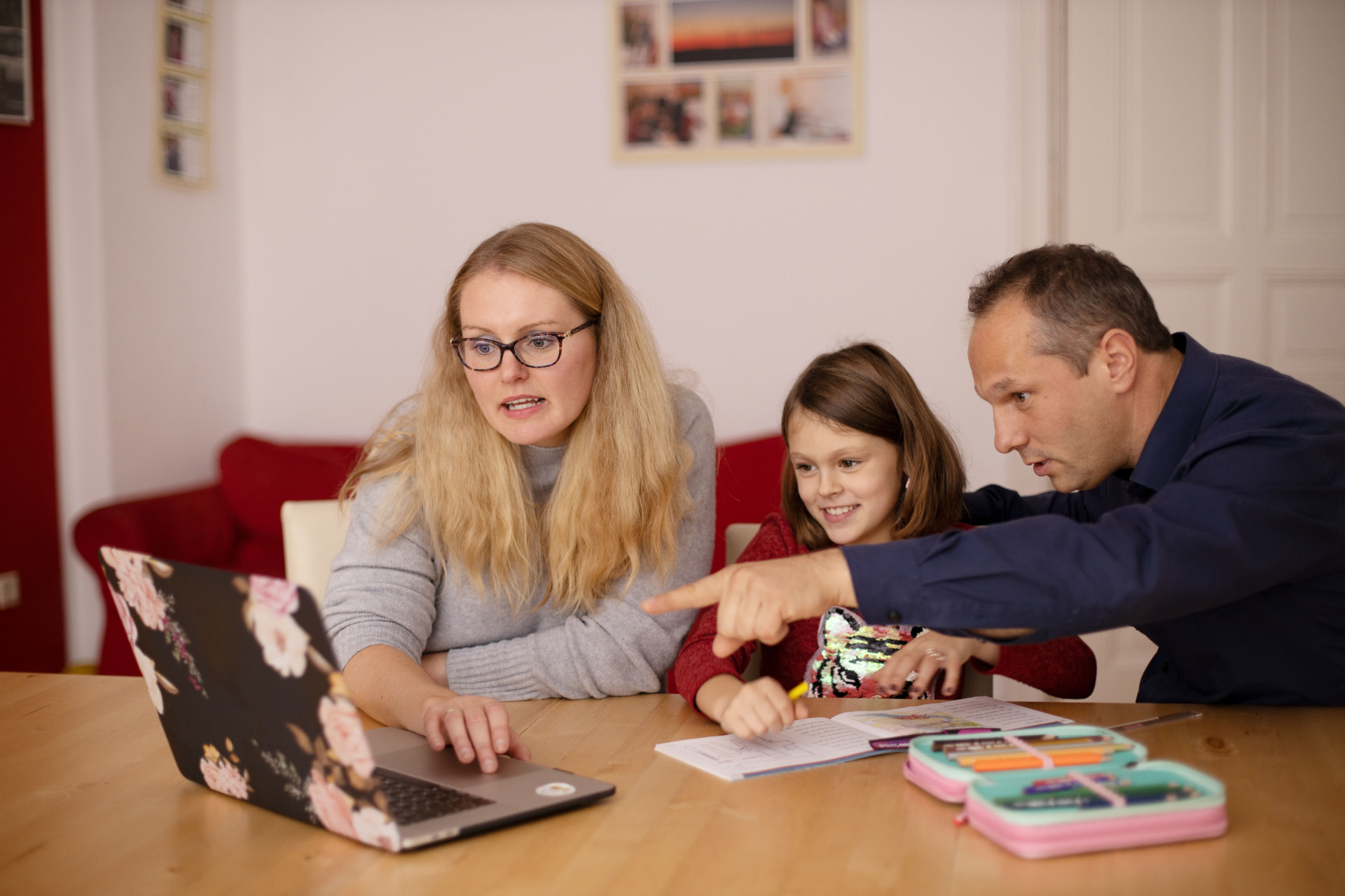 Two parents and their daughter working on schoolwork together at home