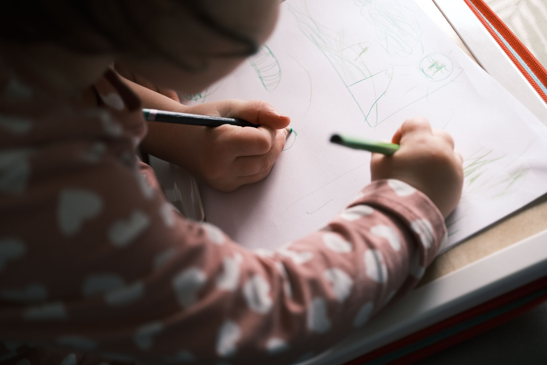 A small child drawing with colored pencils by a sunny window
